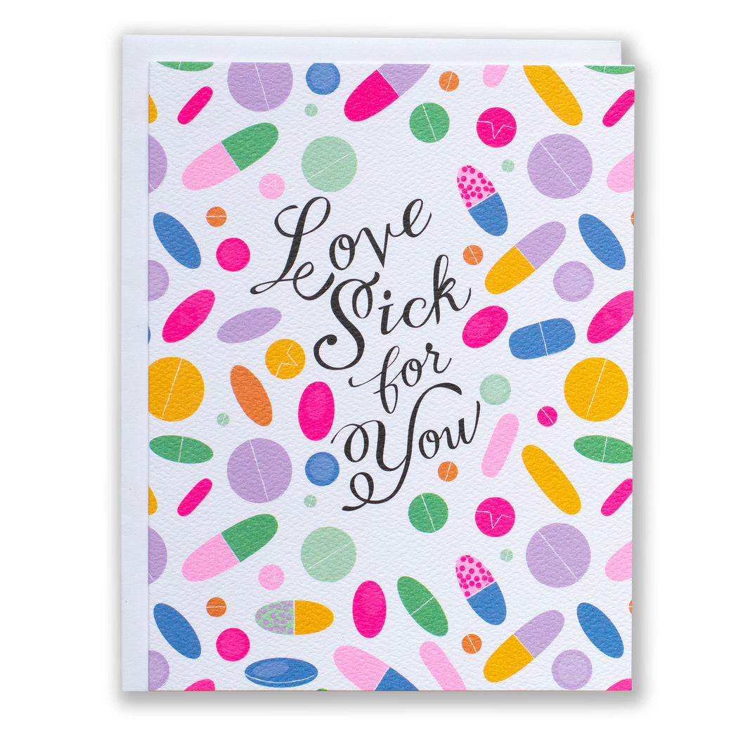 scattering of brightly coloured pills on a  card that reads "Love Sick for You"