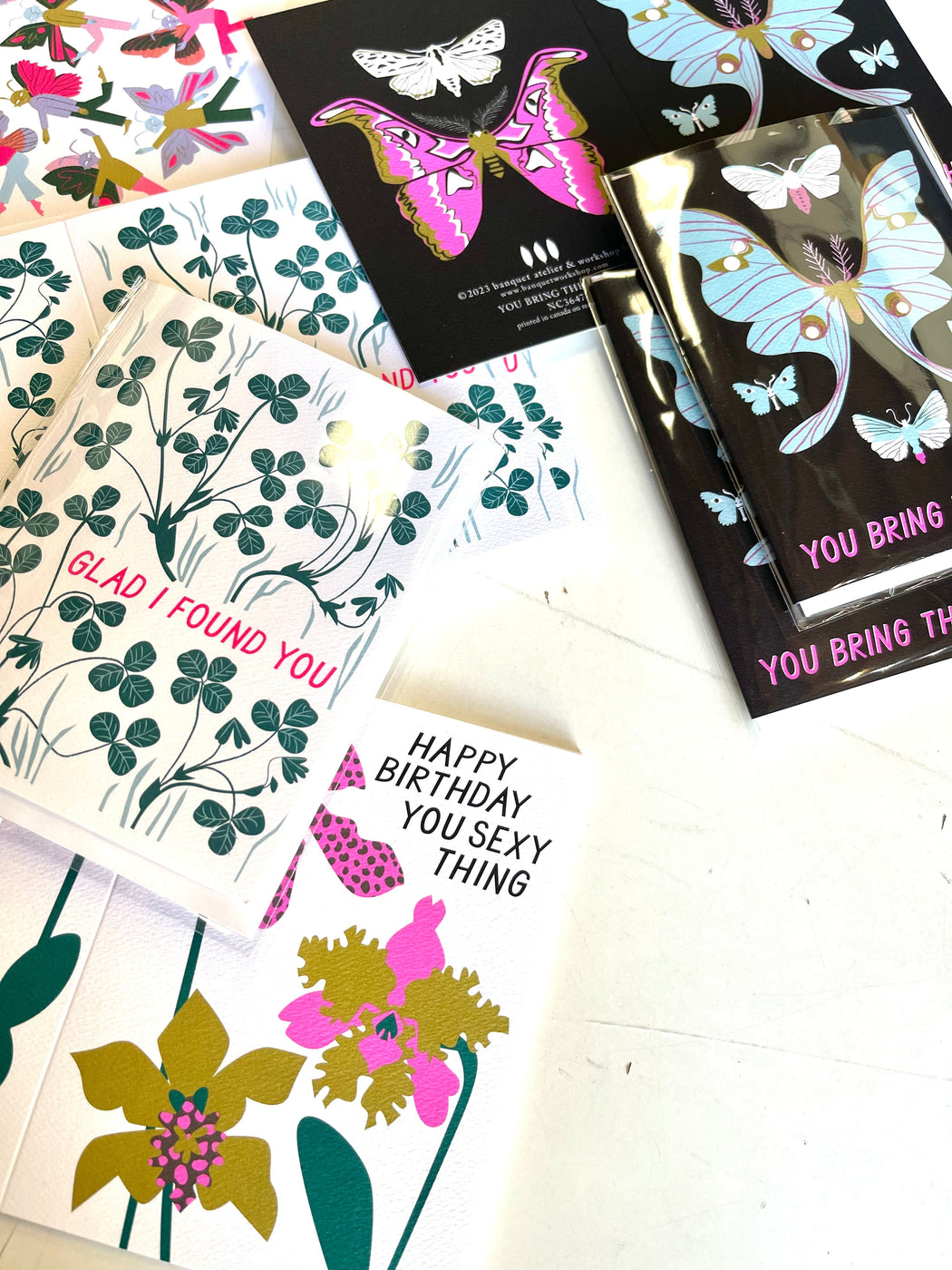 a scattering of note card with hand drawn orchids in neon purple golden green and text in black that say Happy Birthday You Sexy Thing and Glad I Found You clover card and You Bring the Light moth cards