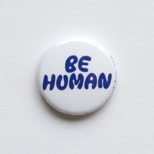 one inch lapel button reads "Be Human" in funny blue lettering